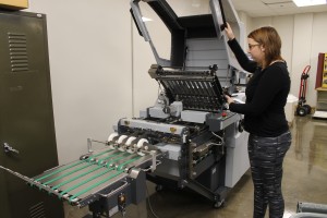 Graphic media management major Erin Deater pops the hood on a machine used to fold mass quantities of paper in the graphic media management print lab