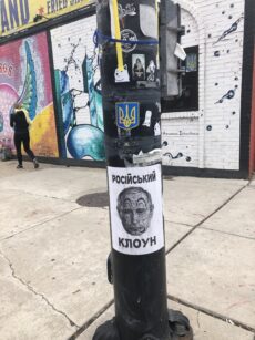 Letter-sized paper affixed to a pole displaying Russian President Vladimir Putin as a clown with the caption "Russian clown" in Ukrainian.