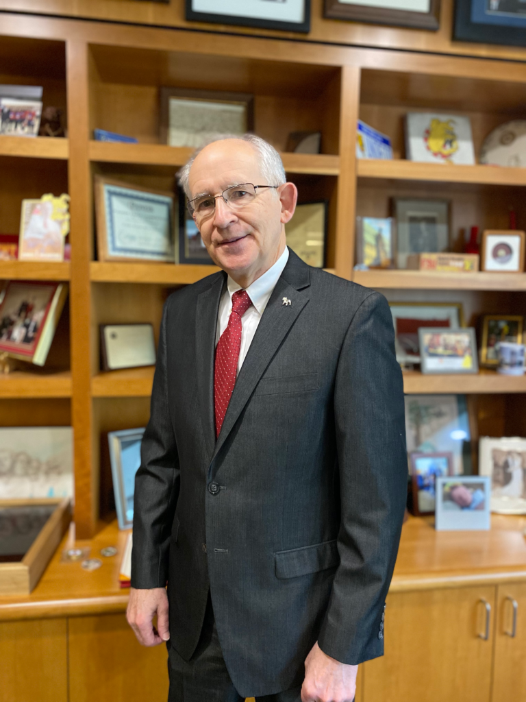 President Eisler stands in front of a book case in his office